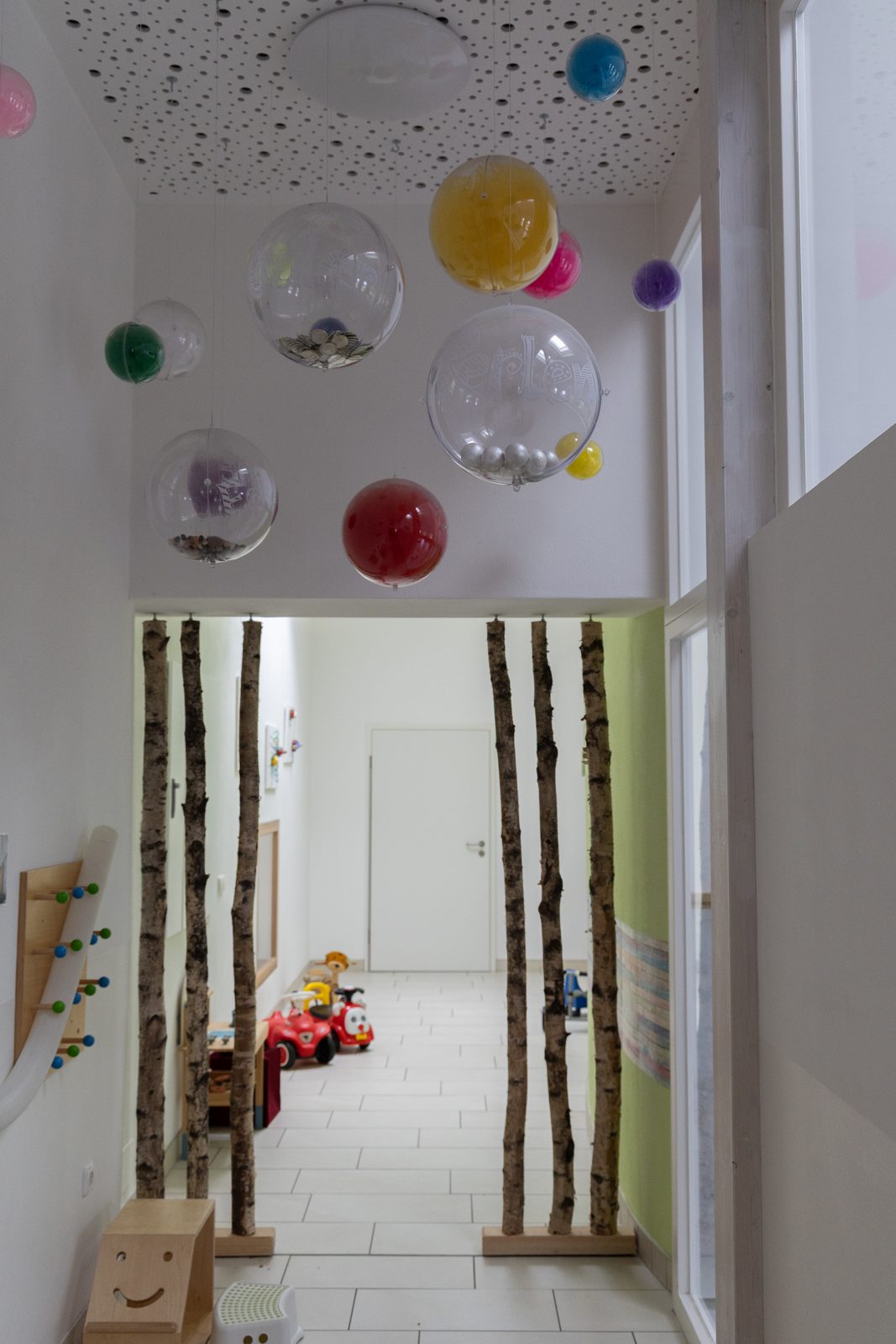 Flur mit Birkenstämmen und bunten Kugeln an der Decke